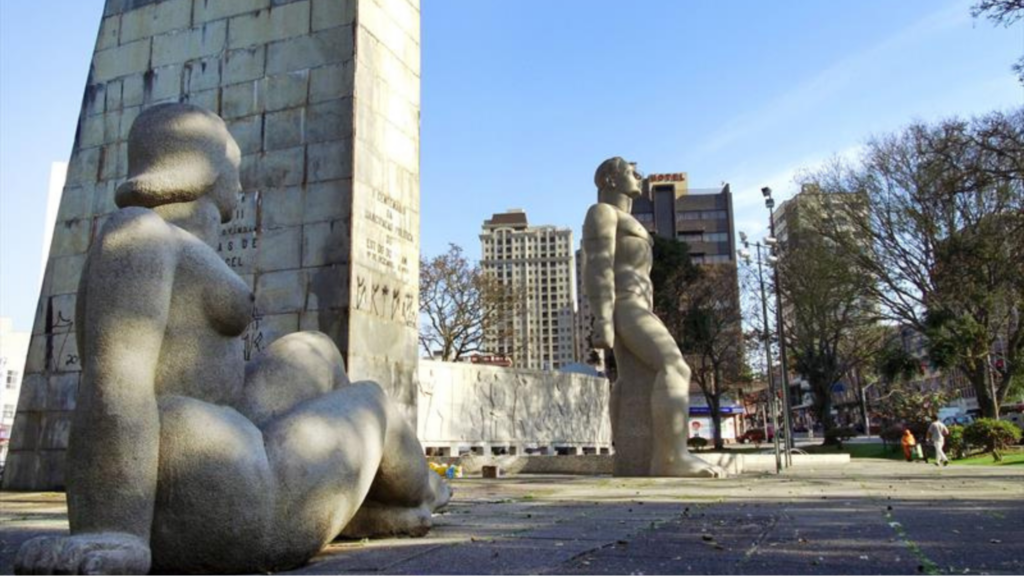 Monumentos na Praça 19 de Dezembro. O Homem Nu, de Erbo Stenzel, e a Mulher Nua, de Humberto Cozzo, com o Obelisco, ao centro, e um painel, ao fundo, com temas da História do Paraná. (Imagem: Governo de Curitiba)