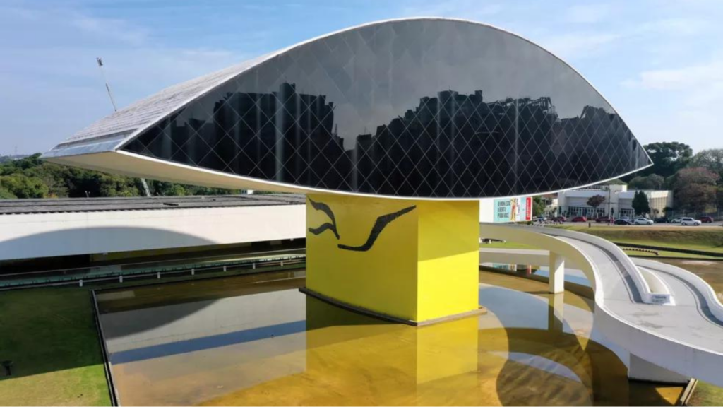 O "Olho iluminado" na época da inauguração do Museu, segundo o projeto original de Oscar Niemeyer. Embaixo, o interior do "Grande Salão do Olho" como era. Via-se o maravilhoso teto com os laminados suspensos. Embaixo, à esquerda, o salão atual rico em obras de arte. (Imagem: G1)